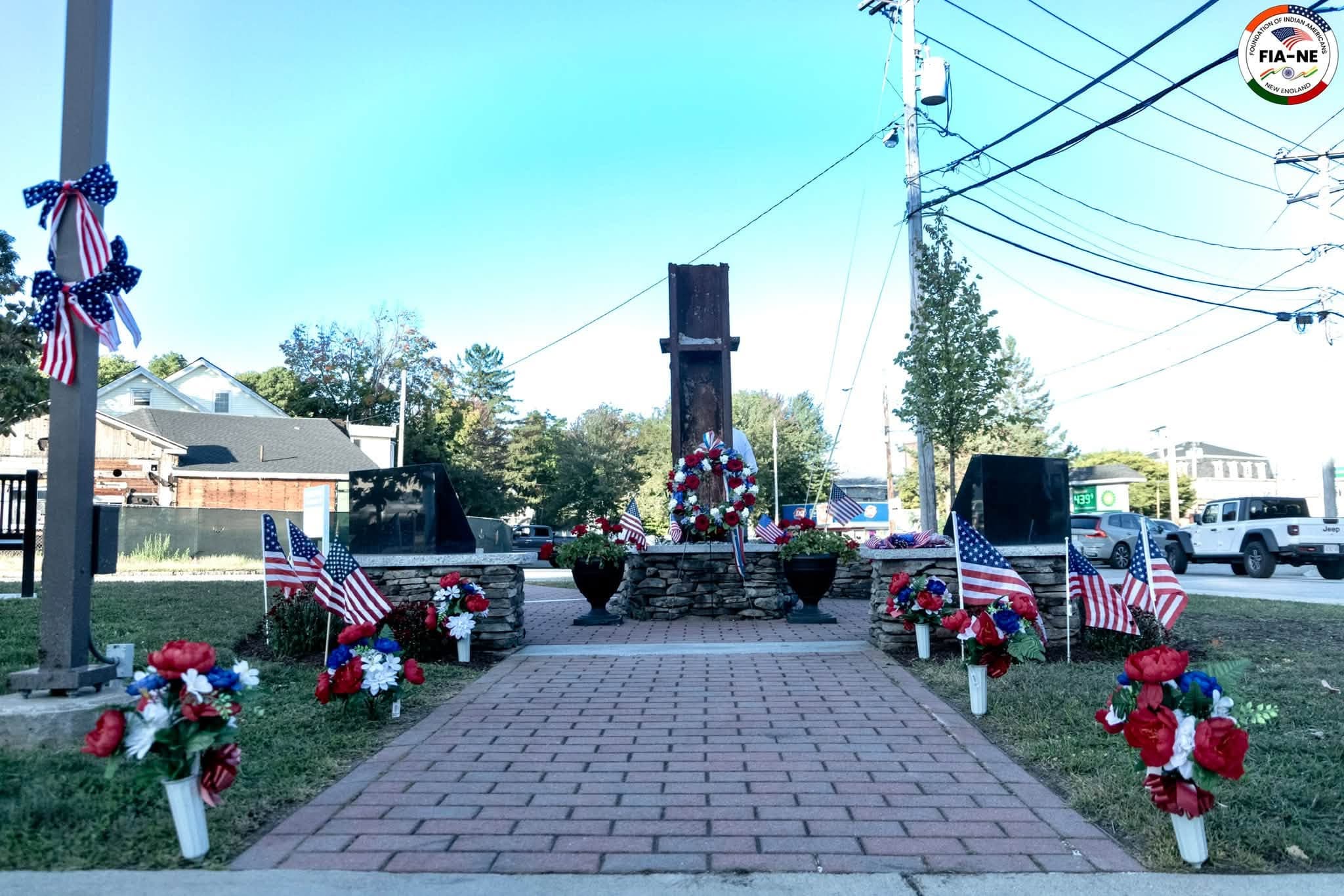 Wreaths of red, white, and blue flowers and small American flags at the base of the steel-beam 9/11 memorial outside the Westborough Fire Station